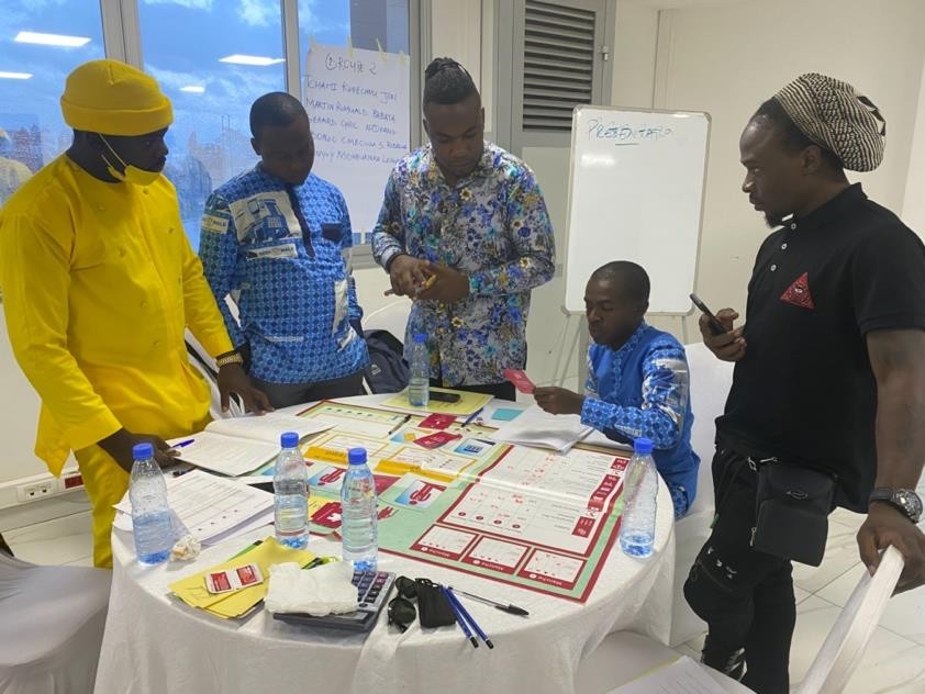 Cuhlia musicians gathered around a business-game board during a training session