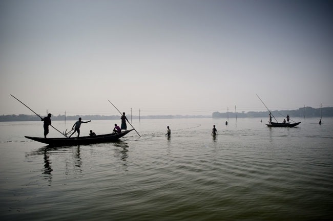 Fishermen poling boats across floodwater at dawn